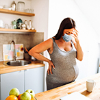 Pregnant woman standing at kitchen counter appearing distressed.