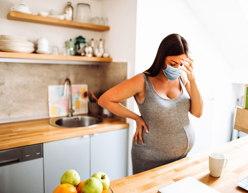 Pregnant woman standing at kitchen counter appearing distressed.