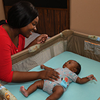 Mother next to baby placed to sleep on his back in a safety approved bassinet.