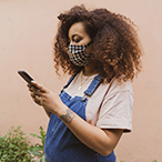 Pregnant woman wearing mask checking mobile device.
