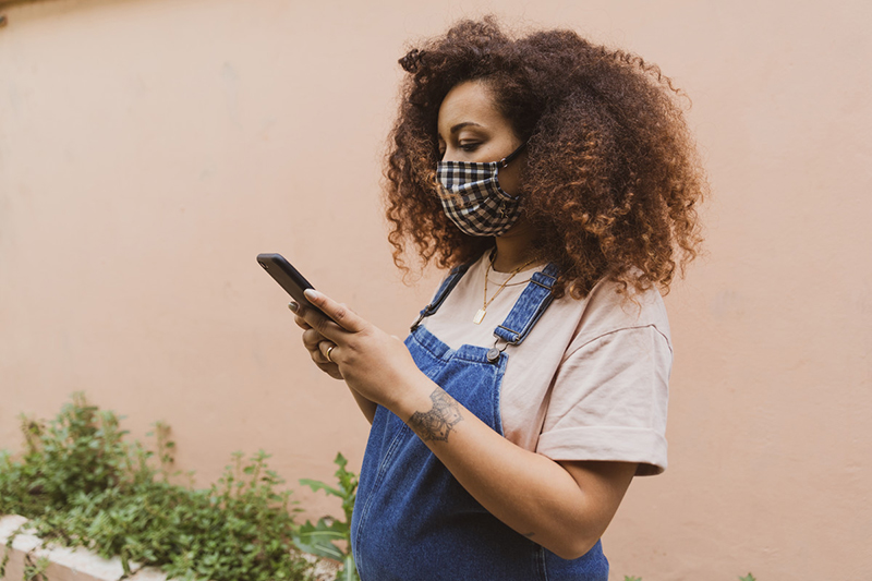 Pregnant woman wearing mask checking mobile device.