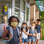 Masked children lined up outside school building.