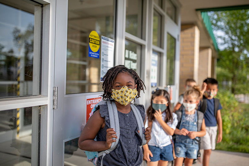 Masked children lined up outside school building.