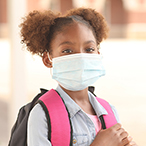 Elementary school-age Black/African American girl with backpack and wearing mask.