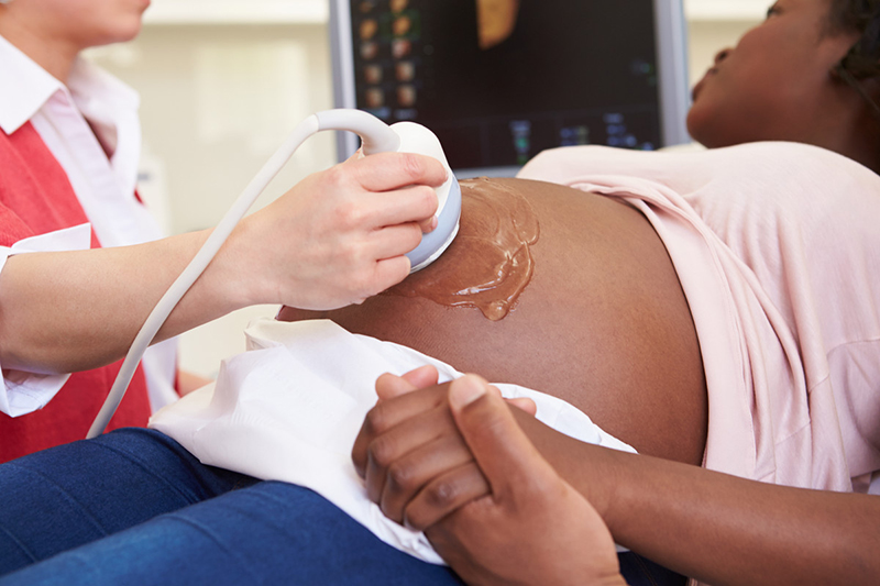 A technician passes an ultrasound transponder over a pregnant woman’s abdomen.