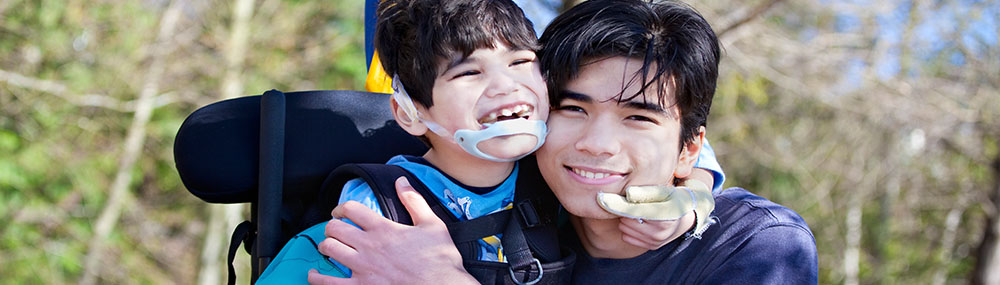 Young boy with cerebral palsy hugging an older boy and laughing.