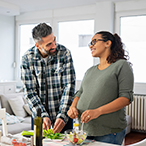 Man and pregnant woman standing over table preparing salad.