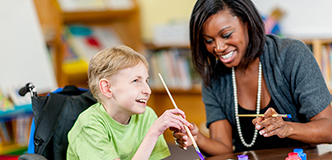 A woman and a boy with a physical disability laughing together while painting.
