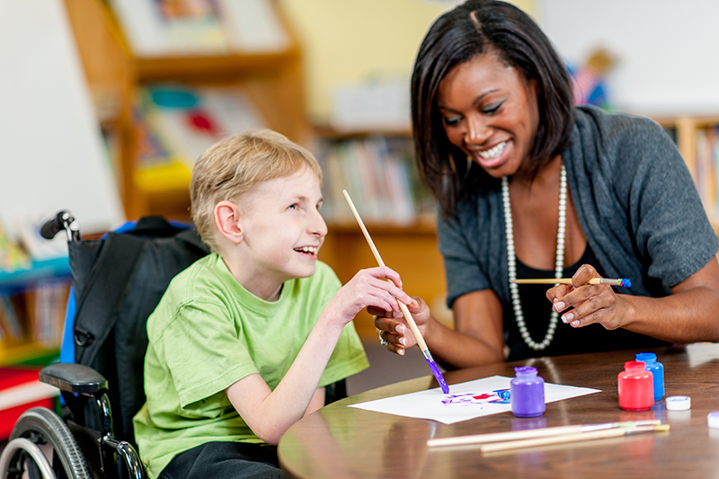 A woman and a boy with a physical disability laughing together while painting.