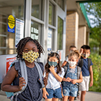 Masked children lined up outside school building.