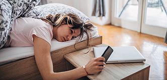 Woman lying in bed looking at cell phone.