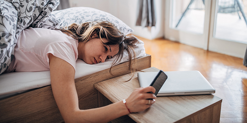 Woman lying in bed looking at cell phone.