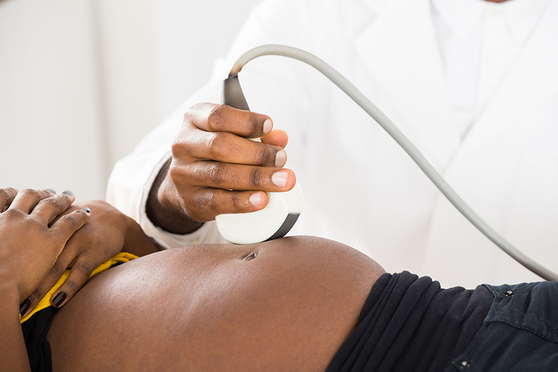 Healthcare provider's hand moving ultrasound on a pregnant woman’s belly.