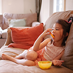 Girl sitting on couch eating snack food from a bowl.