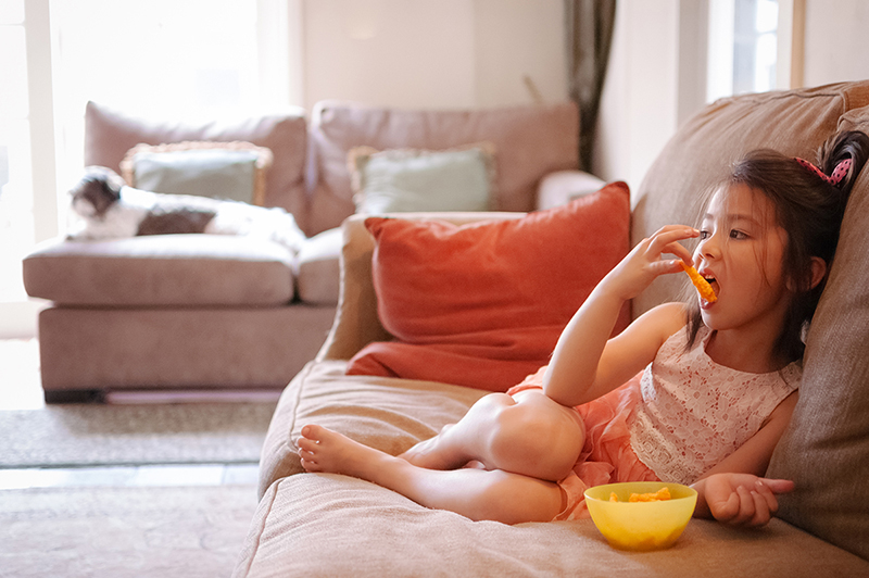 Girl sitting on couch eating snack food from a bowl.