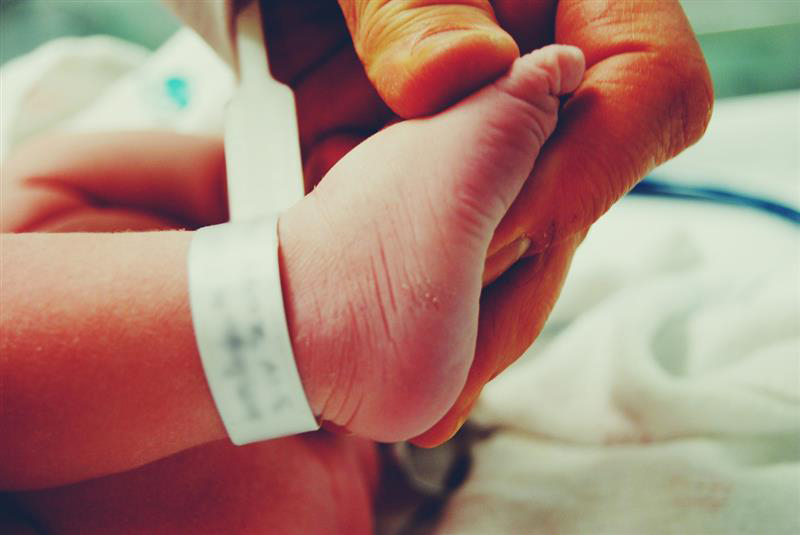 Hand holding infant foot in preparation for a heel stick.