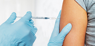 Gloved hand’s injecting a hypodermic needle into a woman’s arm.