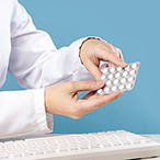 Hands holding hormonal contraceptive pills over computer keyboard.
