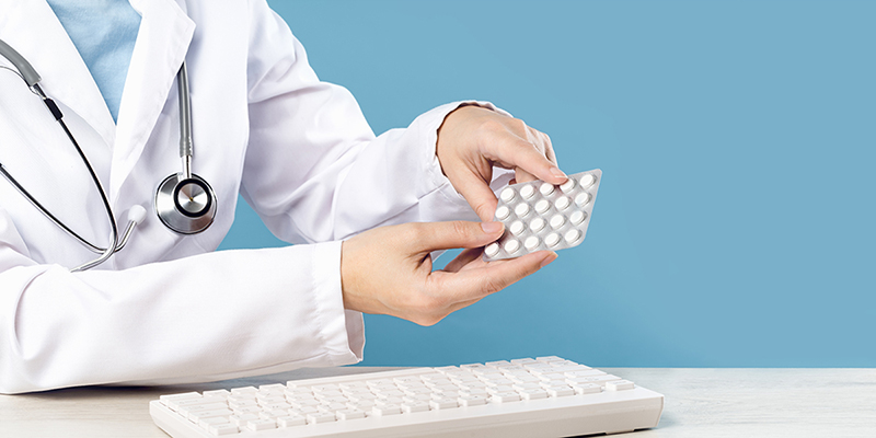 Hands holding hormonal contraceptive pills over computer keyboard.