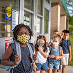 A group of masked children stand outside a school building.