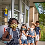 Children are lined up outside a school wearing facemasks.