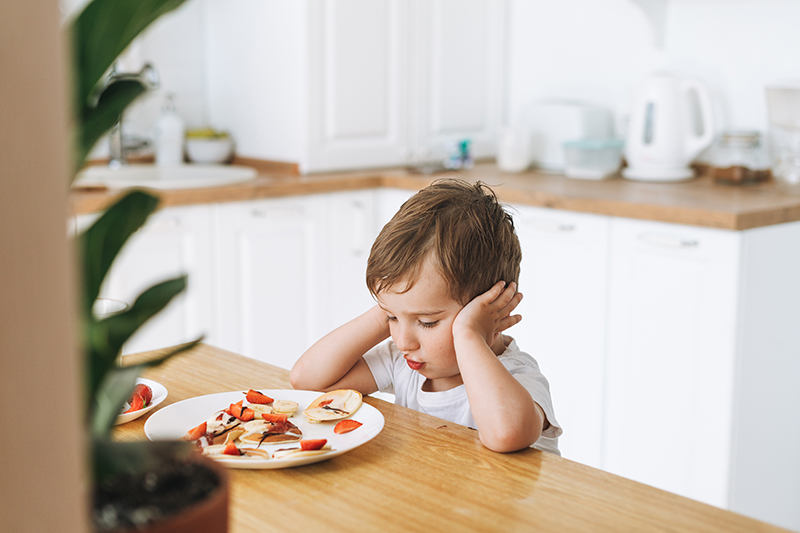 Child sitting at table, looking sadly at plate of food.