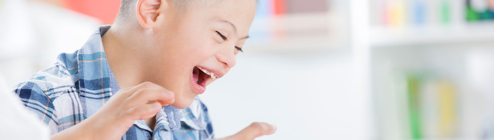 Young boy with Down syndrome laughing.
