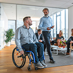 Person in wheelchair talking to standing healthcare worker.