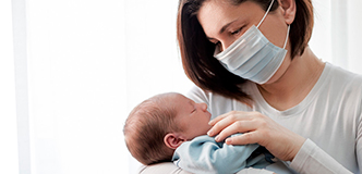 A mother wearing a face mask holds her newborn baby.