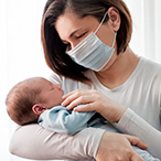 A mother wearing a face mask holds her newborn baby.