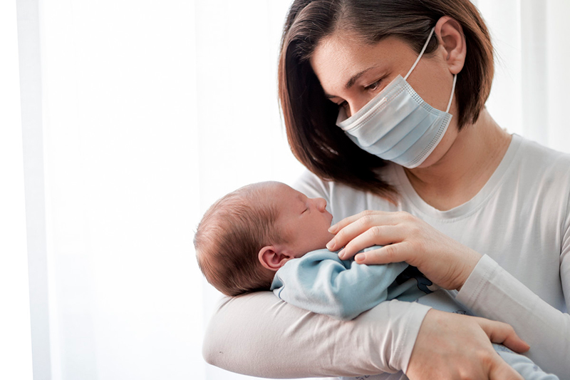 A mother wearing a face mask holds her newborn baby.