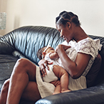 Woman sitting on a couch and breastfeeding an infant.