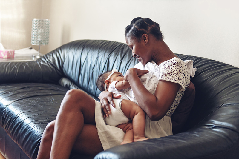 Woman sitting on a couch and breastfeeding an infant.