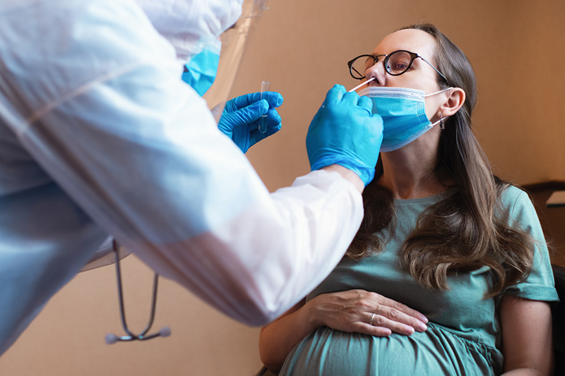 Pregnant person with lowered mask while a technician swabs a nostril.
