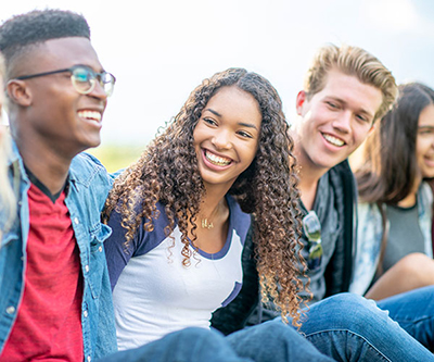 A diverse group of five teenagers are sitting outside smiling.