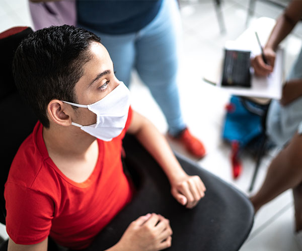 A masked student sits in a wheelchair in a classroom.