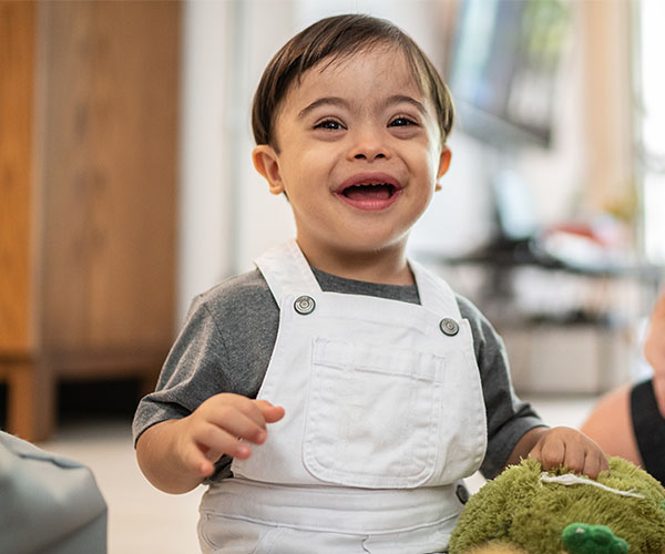 A toddler with Down syndrome smiles as he plays.