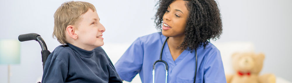 Healthcare professional kneeling to speak with a patient in a wheelchair. 