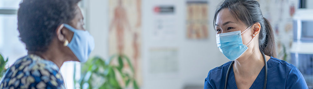 A woman speaking with a healthcare provider in an exam setting. Both people are wearing masks.