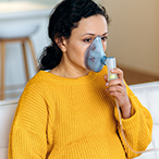 Pregnant woman holding an assistive breathing device to their face.