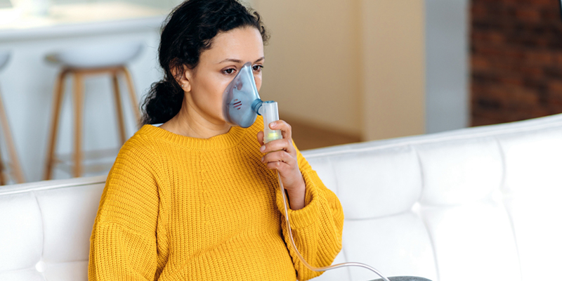 Pregnant person holding an assistive breathing device to their face.