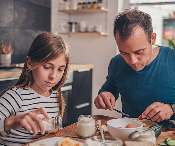 A father and daughter are eating a meal inside their home.