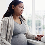 A healthcare provider wearing a white coat holds the hand of a pregnant person while talking with her.