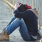 Youth sitting on ground, looking down.