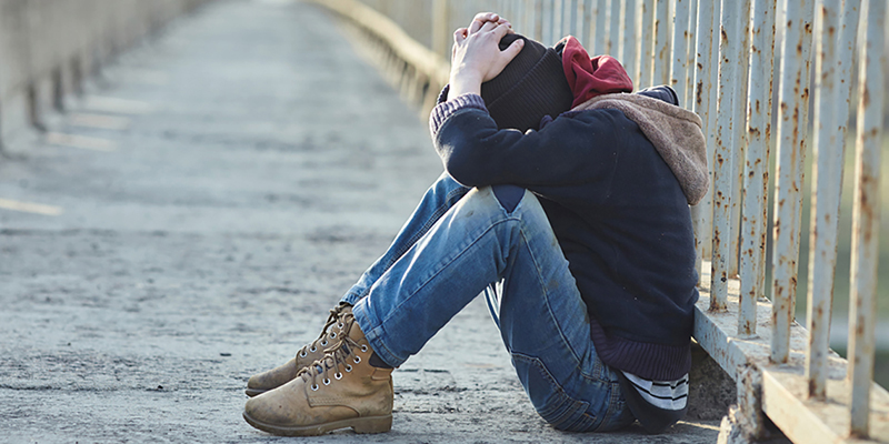 Youth sitting on ground, looking down.