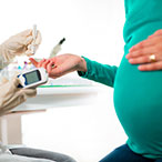 Pregnant woman midsection view, holding finger out for diabetes blood test.