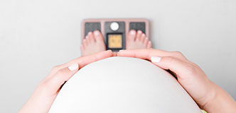 Point of view image of a pregnant person looking down at their feet on a scale.