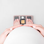 Point of view image of a pregnant person looking down at their feet on a scale.
