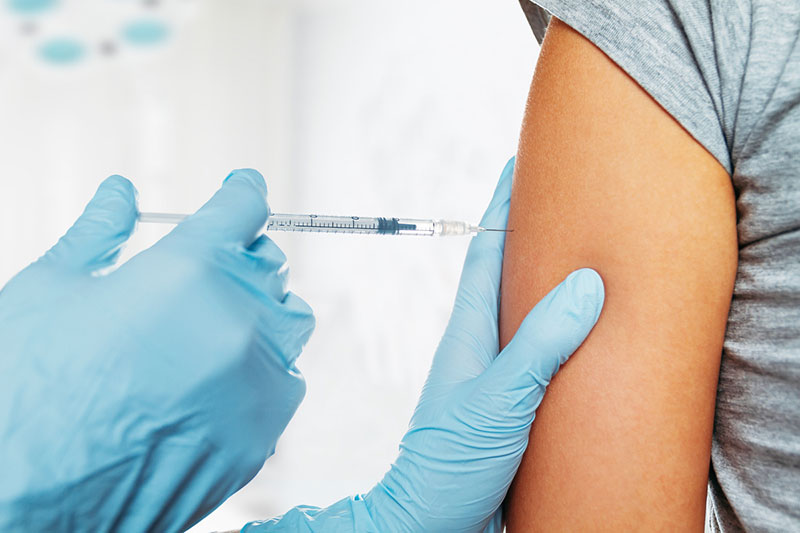 Gloved hands injecting a vaccine into a person’s arm.