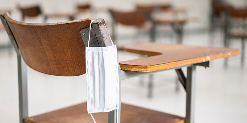 Surgical mask hanging from the seat of a classroom desk.